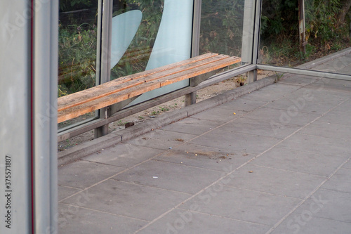 an empty stop with glass walls and a wooden seat for public transport in Europe in the early morning