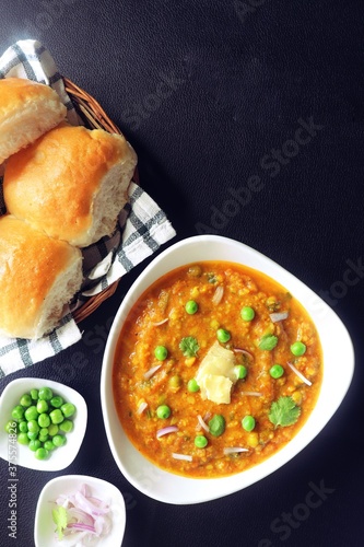 Indian Mumbai Street style Pav Bhaji, garnished with peas, raw onions, coriander and Butter. Spicy thick curry made of out mixed vegetables, served with paav over black background with copy space. 
