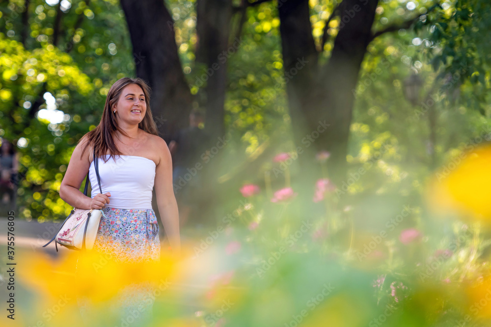 a young woman dressed in a light top and in a variegated skirt walks through the city park a young woman dressed in a light top and in a variegated skirt walks through the city park