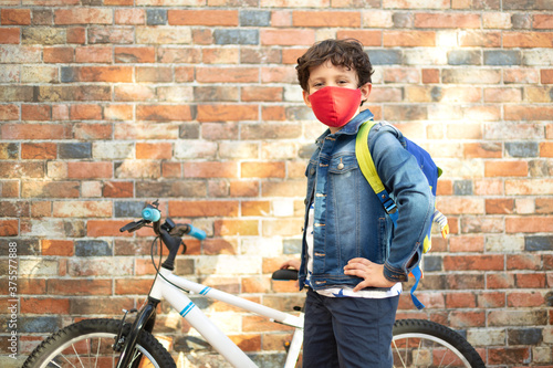 Little boy with his bike ready to go to school. He's on the street and he's wearing a face mask. photo