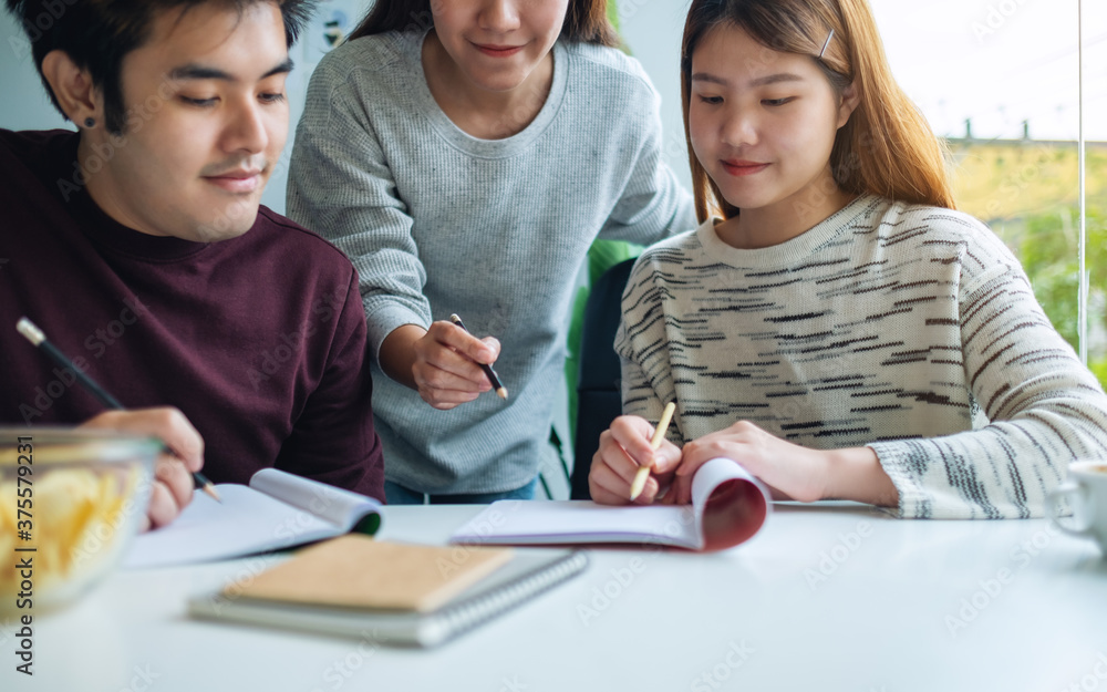 Group of young students tutoring and catching up workbook with friends Group of young students tutoring and catching up workbook with friends