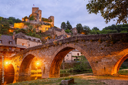 Medieval French Belcastel village with stone arched bridge across Aveyron river and ancient castle on hill in sumer twilight