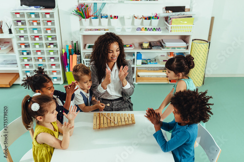 Teacher helping young preschool kids playing musical toys