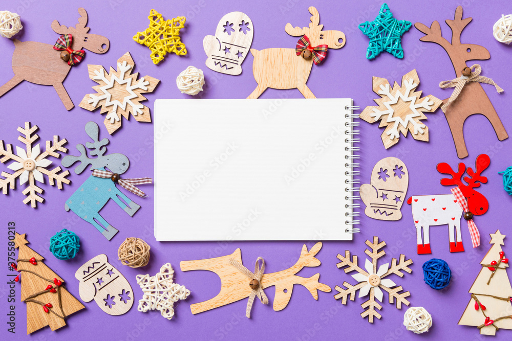 Festive decorations and toys on purple background. Top view of notebook. Merry Christmas concept Festive decorations and toys on purple background. Top view of notebook. Merry Christmas concept