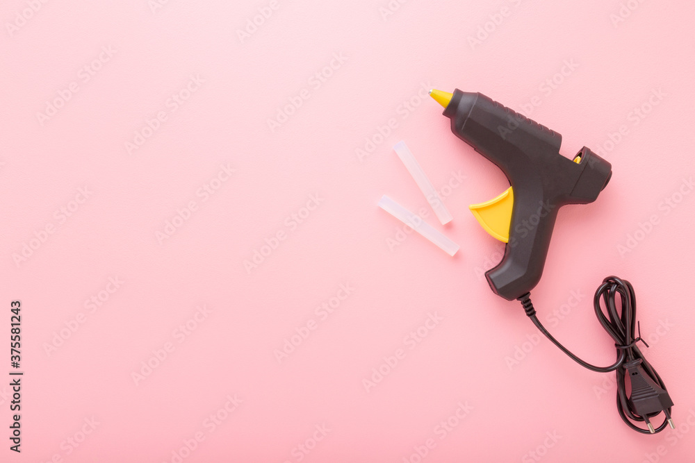 Black glue gun with plastic sticks on light pink background. Pastel color. Closeup. Empty place for text. Top down view. - obrazy, fototapety, plakaty 