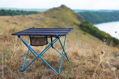 Small folding table stand on the top of the mountain the river background. Tourism equipment in nature in a natural environment. Equipped holiday camp. no bodies. lightweight and compact equipment.
