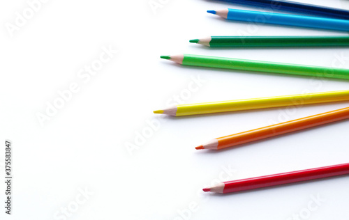 multicolored pencils, rainbow colors, lie chaotically horizontally, to the right, on a light, white background. Scattered multicolored pencils on the right. Subjects for creativity, art school,
