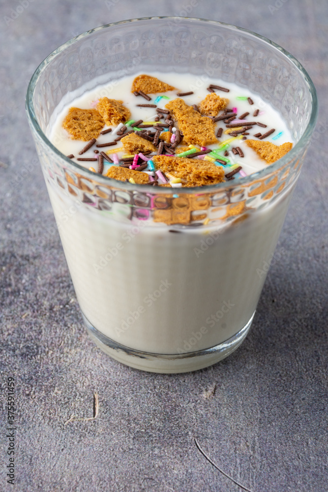 Top closeup of a glass with natural yogurt, biscuit pieces and colors, on gray background, in vertical Top closeup of a glass with natural yogurt, biscuit pieces and colors, on gray background, in vertical