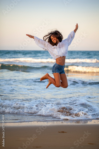 Chica joven saltando contenta en la playa al atardecer