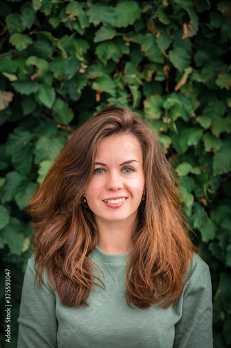 Portrait of a young brunette woman with long hair on a background of green leaves