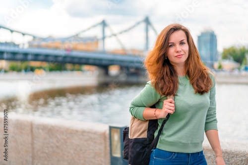 A young brunette woman with a backpack walks along the embankment in Moscow © KseniaJoyg