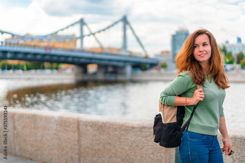 A young brunette woman with a backpack walks along the embankment in Moscow