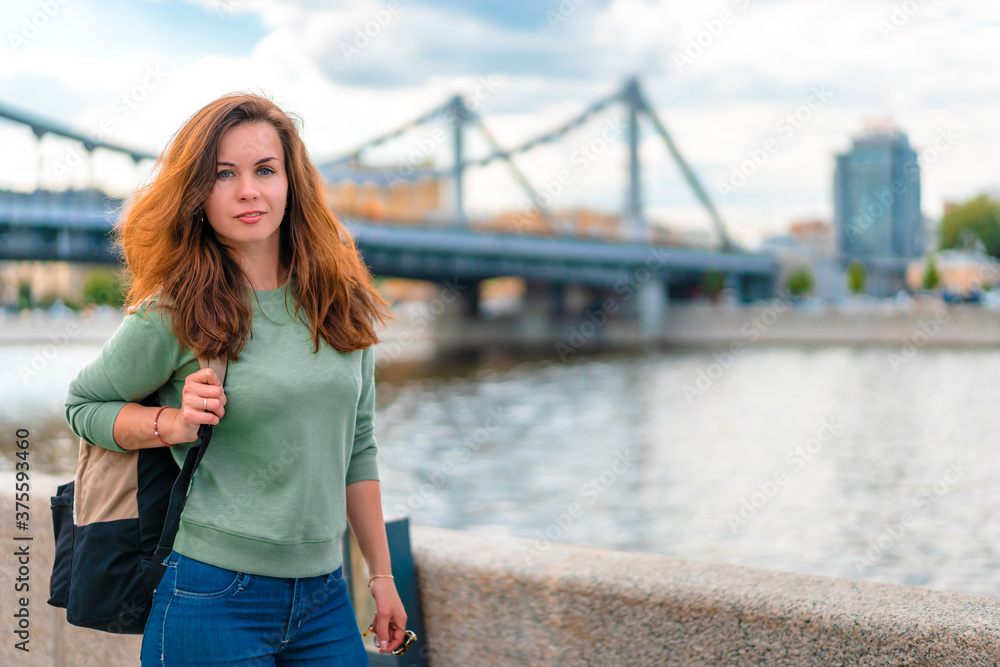 A young brunette woman with a backpack walks along the embankment in Moscow