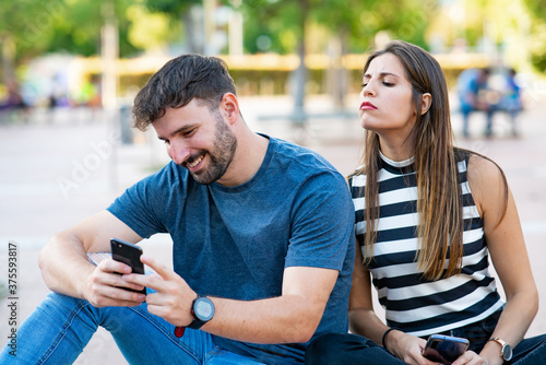 Tableau sur toile Cheating man chatting with women on his smartphone while his girlfriend spies on