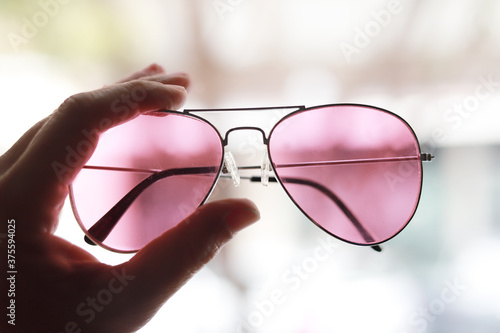 gafas de sol color rosa sujetadas por un lado con un fondo de ciudad fuera de foco