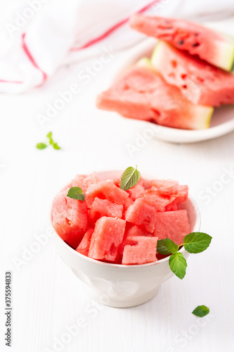 Juicy ripe sweet red watermelon slices with mint leaves in a bowl on a white background, delicious summer berries