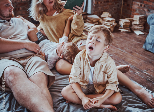 American boys with whole family having a good time at home and reading book with fairytale.