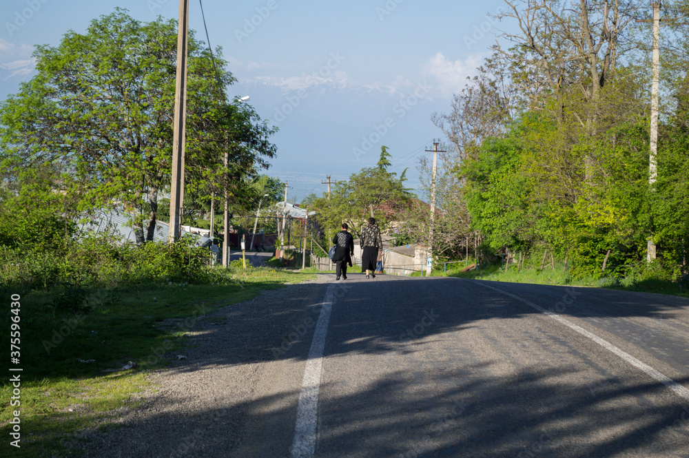 Two Women Walking down a Road in a Small Georgian Village near Sighnaghi with view onto the Caucasus Mountains, Georgia