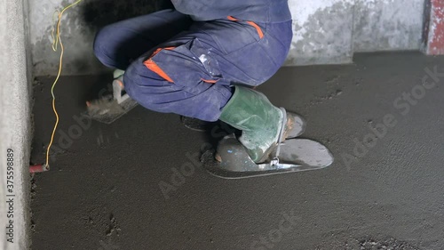 Construction worker kneeling, flattening the cement floor with a hand leveler photo