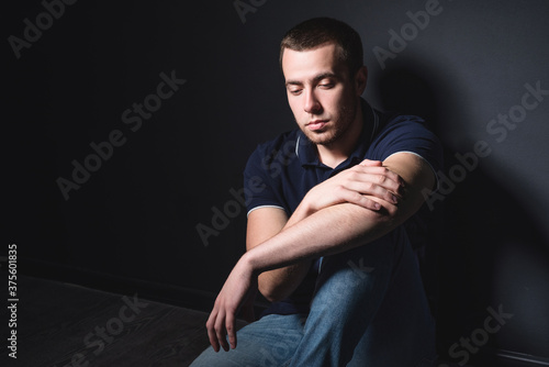 Young attractive man in blue jeans and a polo shirt sits on the floor near the wall in the studio. Youth and attractiveness concept