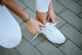 young girl tie her white shoelaces at the street