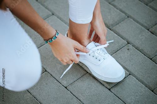 young girl tie her white shoelaces at the street