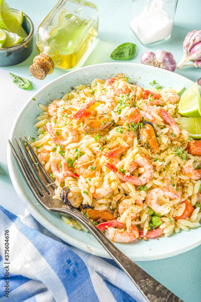 Orzo pasta with cream sauce and seafood. Homemade Orzo with various seafoods and shrimps, with lemon slices on light blue background copy space top vuew Orzo pasta with cream sauce and seafood. Homemade Orzo with various seafoods and shrimps, with lemon slices on light blue background copy space top vuew