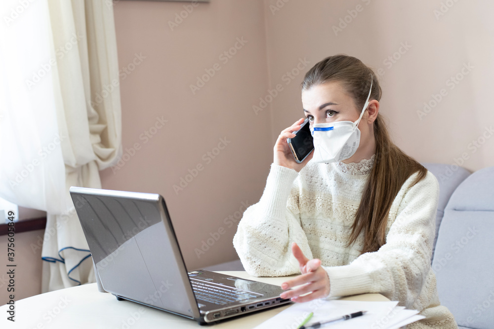 masked girl with telephone, quarantined at home working with laptop masked girl with telephone, quarantined at home working with laptop