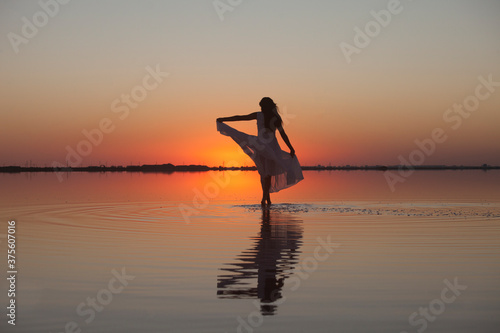 Woman walking on the water silhouette in a beautiful dress on the lake in the evening light at sunset