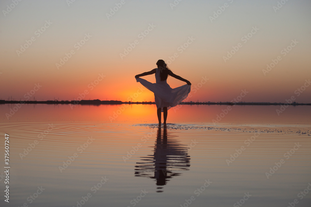 Silhouette of a woman standing in the water in a beautiful dress on the lake in the evening light at sunset