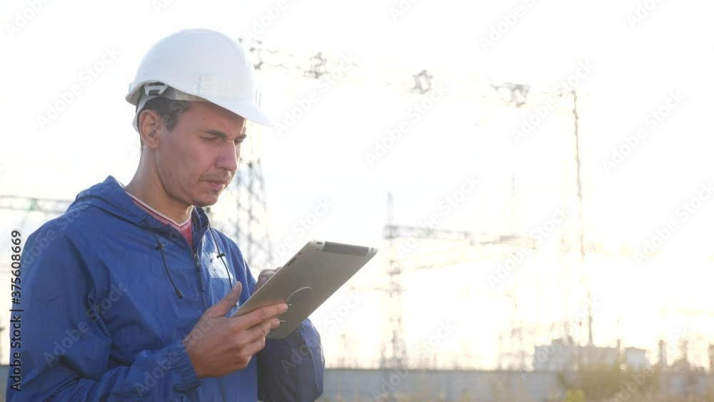 power electrical worker engineer in helmet a working with digital tablet, near tower with electricity. business energy technology industry concept. electrical studying reading documents on tablet power electrical worker engineer in helmet a working with digital tablet, near tower with electricity. business energy technology industry concept. electrical studying reading documents on tablet