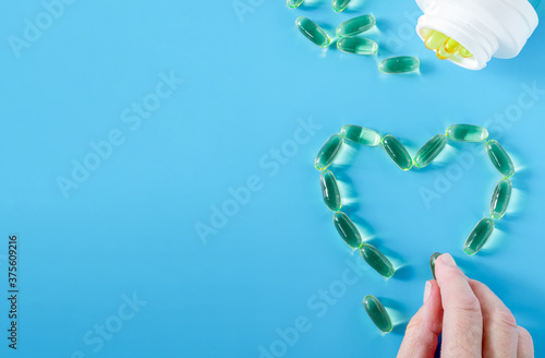 A woman's hand lays out the symbolic outline of a heart from capsules with fish oil. Health, super food concept. Horizontal orientation, selective focus, copy space