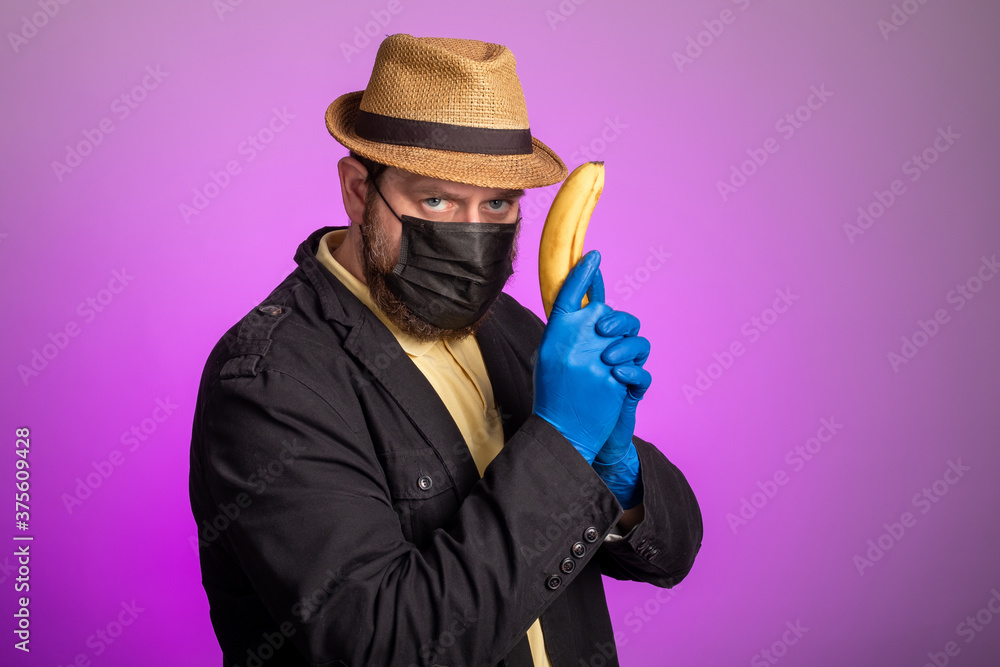 a man in a mask and a hat holds a banana in his hands like a gun a man in a mask and a hat holds a banana in his hands like a gun