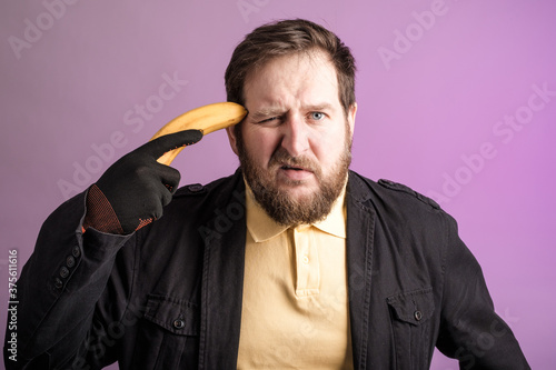 a bearded man held a banana to his head like a pistol photo