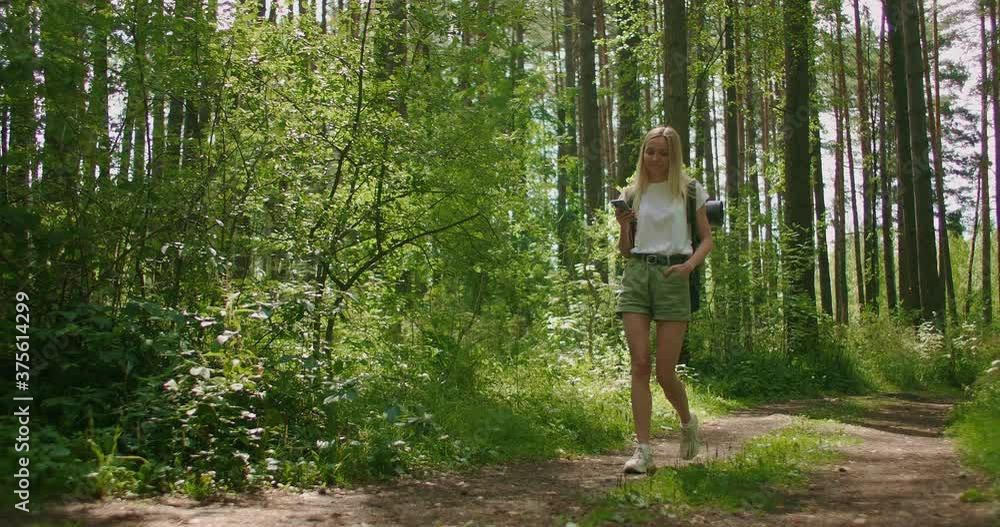 Attractive woman relax in forest and using smartphone outdoors. Woman Hiking In The Forest And Typing Message On Smartphone. Solo female hiker using smart phone. Attractive woman relax in forest and using smartphone outdoors. Woman Hiking In The Forest And Typing Message On Smartphone. Solo female hiker using smart phone.
