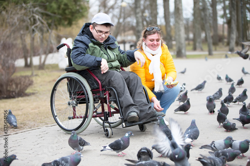 Man in a wheelchair with his wife is feeding pigeons
