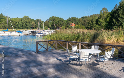 Lounge area for rest and relaxation on wooden pier jetty near a private residence. White outdoor furniture table and chairs for meditation watching the sea and sunset. Yachting people luxury lifestyle