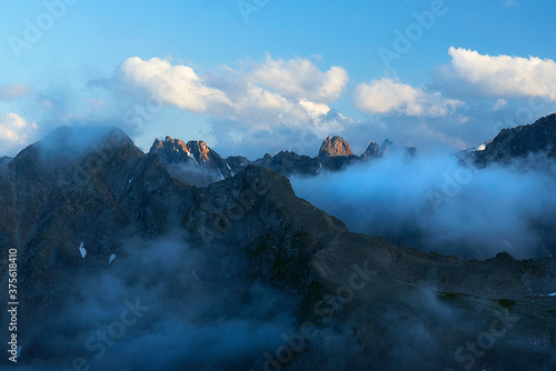 Mountain peaks and mountain gorge with clouds in the evening in blue light. Teberda Nature Reserve, Dombay, Russia. © Ambartsumian