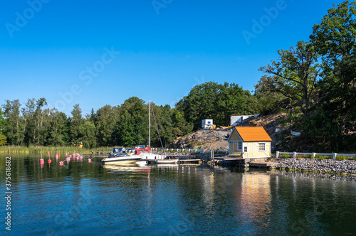 A small yellow wooden house on the shore. Marina berth for private yachts and boats. Jetty for ships near the Coast Of Sweden. The Stockholm archipelago. Active lifestyle yachting.