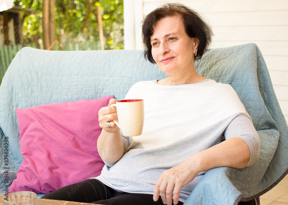 Portrait of dreamy senior woman enjoying drinking coffee in the morning sitting on sofa on home terrace on green garden background.Happy morning routine,day planning,enjoying life,to be in the moment Portrait of dreamy senior woman enjoying drinking coffee in the morning sitting on sofa on home terrace on green garden background.Happy morning routine,day planning,enjoying life,to be in the moment