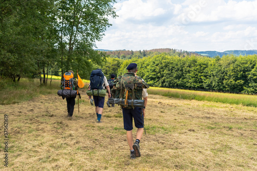 Photography Scouts or tourists go with big backpacks on the green forest trail on sunny summer day