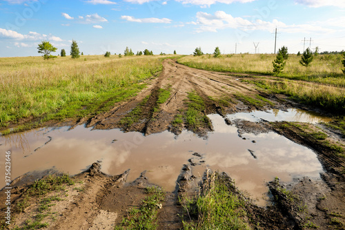 Summer landscape - field road with a large puddle and mud among meadows. The serenity of the countryside.