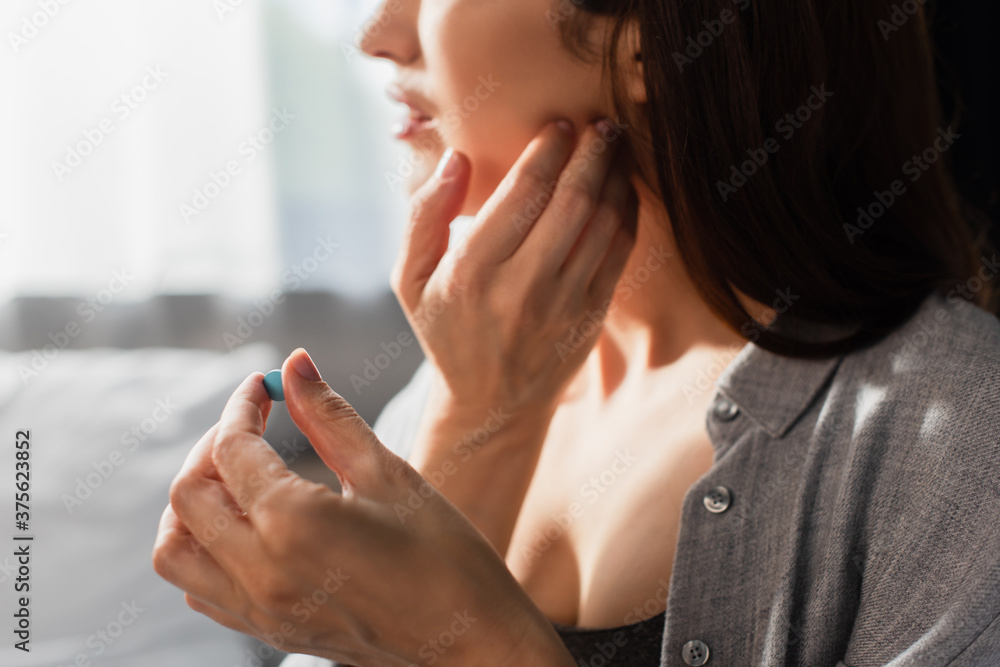 partial view of woman touching face while suffering from toothache and holding pill at home partial view of woman touching face while suffering from toothache and holding pill at home