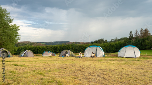 Children kids scouts sit near tents at the base camp. Lots of  tents stand on a field against a green forest. ScoutingTravel Tourism Hiking Trekking Vacation Active lifestyle. 