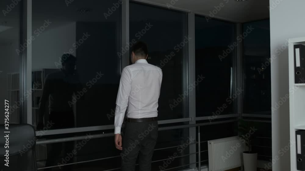 A young lawyer lingered at work until night standing by a panoramic window and talking on the phone A young lawyer lingered at work until night standing by a panoramic window and talking on the phone