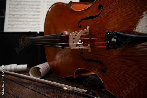 The cello lies on a wooden surface with a bow and music stand. Place for text