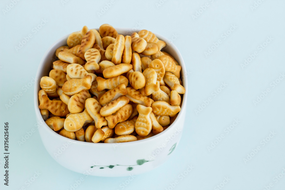 Mini fish shaped crackers heap in the white porcelain plate on light blue surface with copy space Mini fish shaped crackers heap in the white porcelain plate on light blue surface with copy space