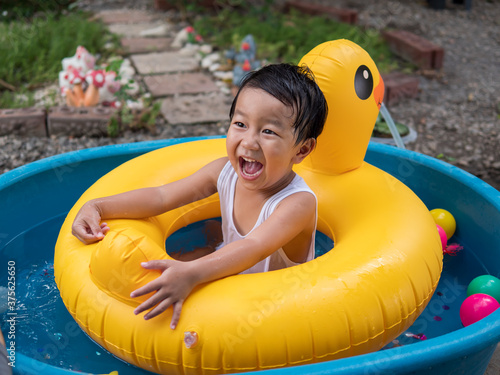 Asian cute child boy laughing while playing outdoor in yellow duck rubber band with rural nature background. Young kid having happy moment in summer. Family activity at home and preschool concept. © Namphueng