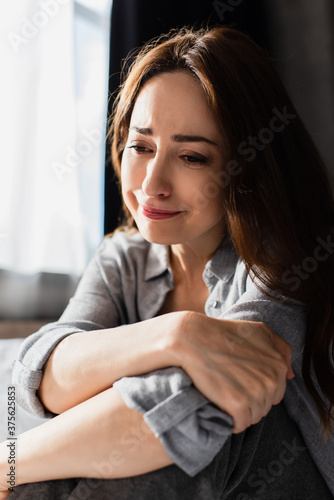 upset and brunette woman touching hand while sitting and crying at home