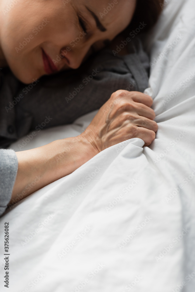 top view of frustrated and brunette woman touching bedding while crying on bed